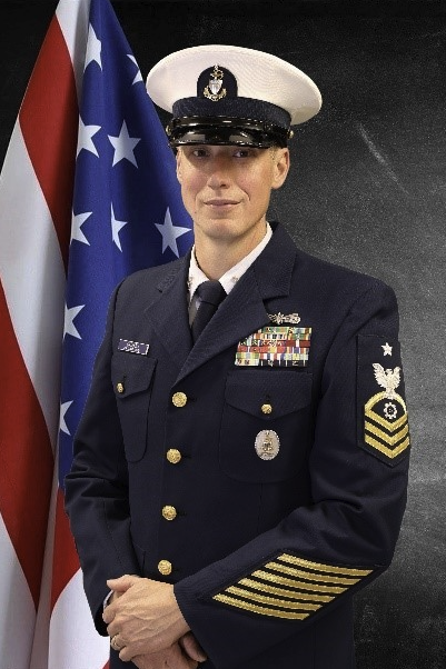 U.S. Coast Guard Senior Chief in service dress uniform standing before U.S. flag